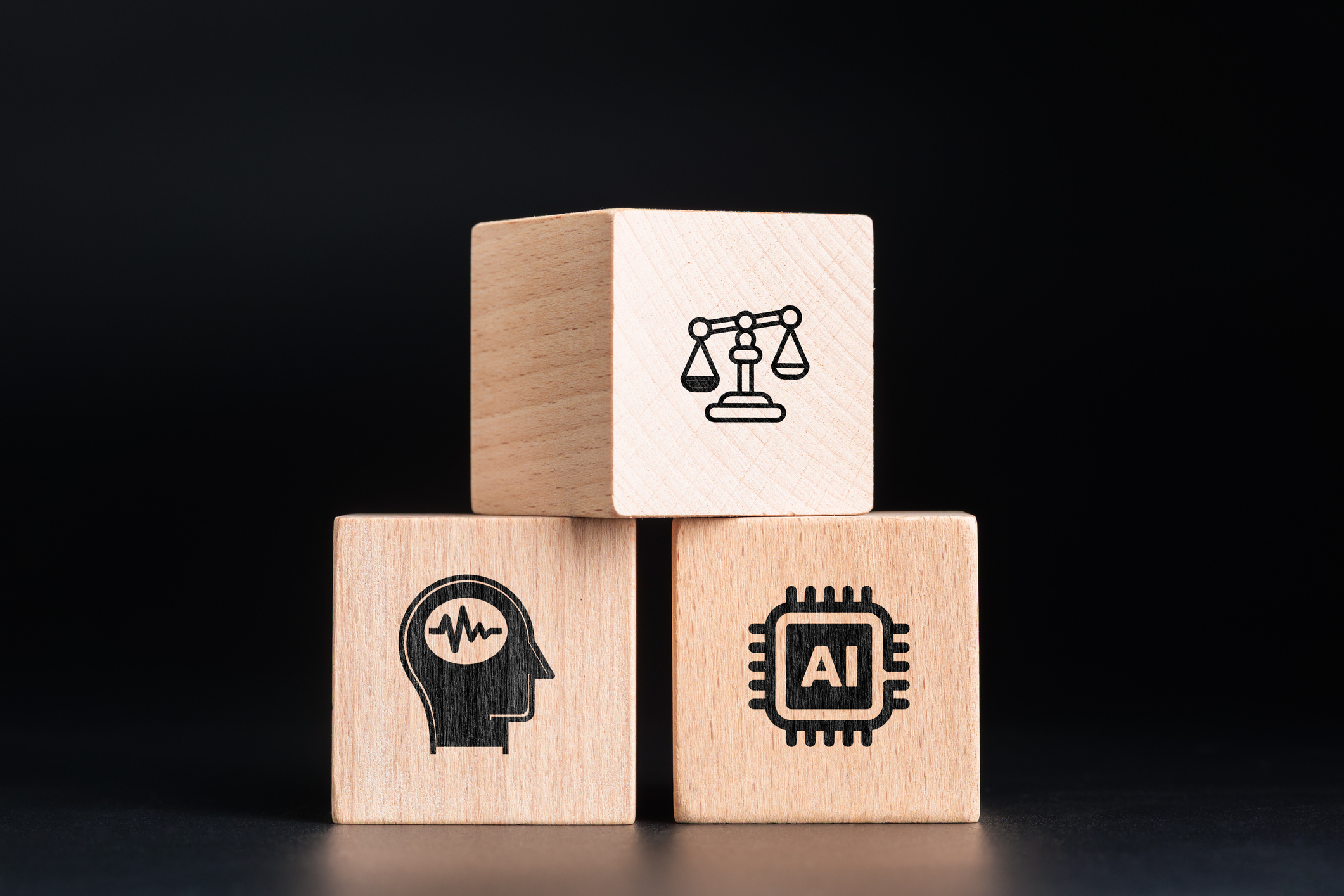 Stacked wooden cubes, one on top of two, depicting the balance between human thought and AI. They blocks show scales on top and human thought and AI on the bottom.